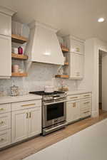 Kitchen featuring open shelves, stainless steel range with gas cooktop, light wood-style flooring, white cabinetry, and tasteful backsplash