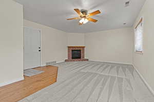 Unfurnished living room featuring ceiling fan, a brick fireplace, light carpet, and light wood-type flooring