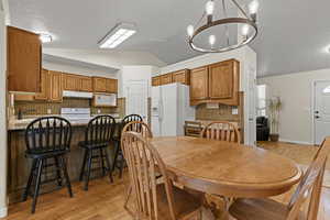 Dining area with vaulted ceiling, light wood finished floors, and a chandelier