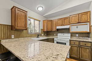 Kitchen featuring wood finish cabinets, a wainscoted wall, a breakfast bar area, white electric stove, and vaulted ceiling