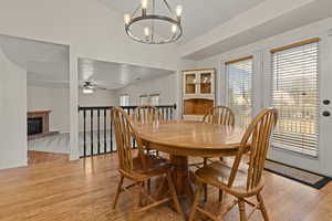 Dining room with a fireplace, light wood-style floors, a chandelier, a ceiling fan, and lofted ceiling