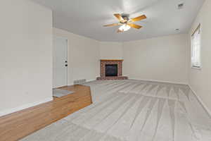 Unfurnished living room featuring ceiling fan, a brick fireplace, light wood-type flooring, and light carpet