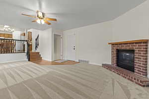 Unfurnished living room featuring light colored carpet, a brick fireplace, ceiling fan, and suspended lighting