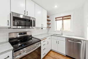 Kitchen with stainless steel appliances, white cabinetry, open shelves, decorative backsplash, and light stone counters