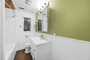Full bath featuring vanity, bathing tub / shower combination, a wainscoted wall, and dark tile patterned floors