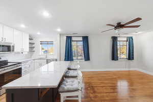 Two tone kitchen with stainless steel appliances, open shelves, tasteful backsplash, light stone counters, and light wood-style flooring