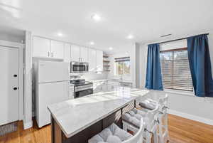 Kitchen featuring stainless steel appliances, open shelves, a breakfast bar area, light wood-type flooring, and white cabinets