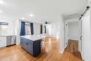 Kitchen with a barn door, a center island, light wood-style floors, a breakfast bar, and stainless steel dishwasher