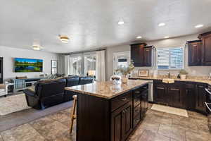 Kitchen featuring a large island, dark wood finish cabinetry, open floor plan, light stone counters, and a kitchen island