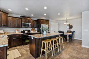 Kitchen featuring stainless steel appliances, dark wood finish cabinetry, a kitchen island, light stone countertops, and a breakfast bar