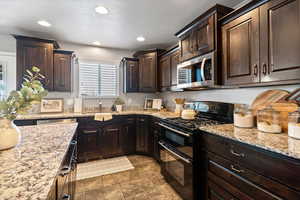 Kitchen featuring dark wood finish cabinetry, double oven range, stainless steel microwave, light stone counters, and recessed lighting