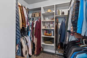 Primary walk in closet with dark colored carpet