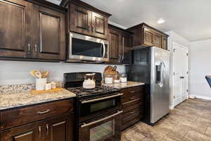 Kitchen featuring stainless steel appliances, dark wood finish cabinetry, light stone counters, and recessed lighting