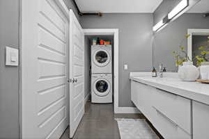 Bathroom featuring vanity, stacked washer and dryer, and dark tile patterned flooring