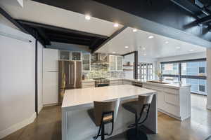 Kitchen with recessed lighting, a peninsula, stainless steel appliances, white cabinetry, and a kitchen bar