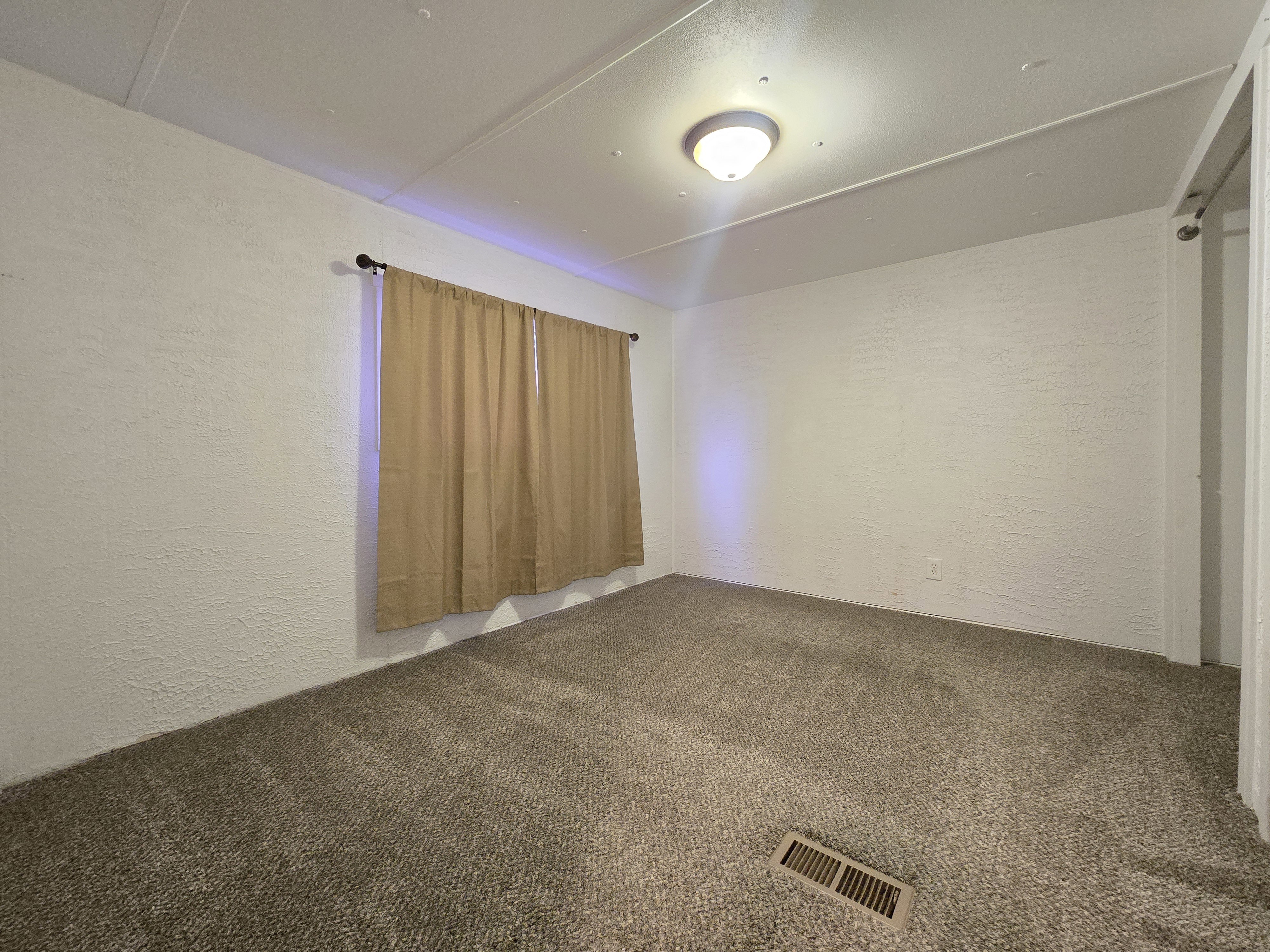 Carpeted room featuring a ceiling-mounted light fixture, textured walls, and a window with a curtain rod