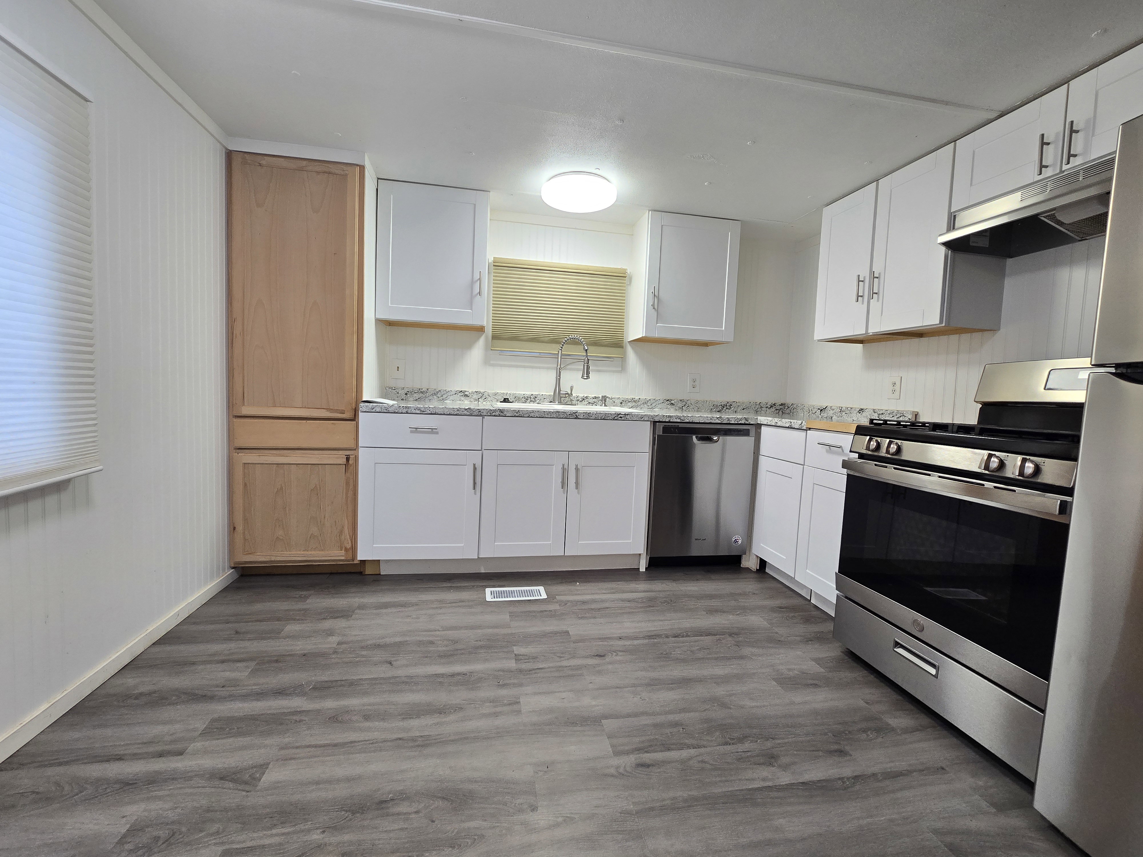 Kitchen featuring white cabinetry, stainless steel appliances, speckled countertops, a double basin sink with a gooseneck faucet, and wood-finish flooring