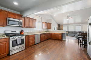 Kitchen featuring stainless steel appliances, a peninsula, open floor plan, wood finish cabinetry, and dark wood-type flooring