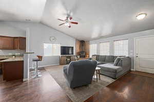 Living area with dark wood finished floors, ceiling fan, a wood stove, and vaulted ceiling