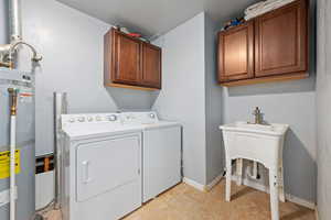 Laundry room featuring secured water heater, cabinet space, washing machine and dryer, and light tile patterned floors