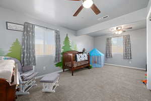 Carpeted bedroom featuring a nursery area and a ceiling fan