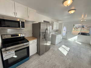 Kitchen with stainless steel appliances, white cabinets, light marble finish floors, decorative backsplash, and washing machine and dryer