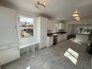 Kitchen featuring white cabinetry, light marble finish flooring, backsplash, and stainless steel dishwasher
