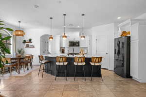 Dual tone kitchen featuring arched walkways, a breakfast bar area, fridge with ice dispenser, a kitchen island with sink, and two tone color scheme