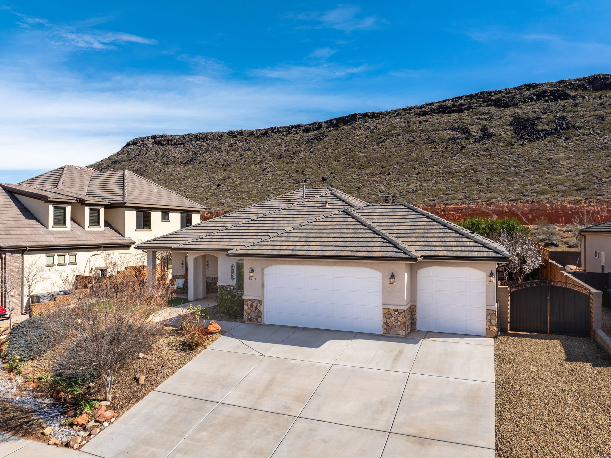 View of front of house featuring a garage, concrete driveway, stone siding, stucco siding, and a gate