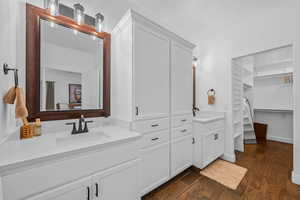 Full bath featuring a walk in closet, two vanities, and dark wood-style flooring