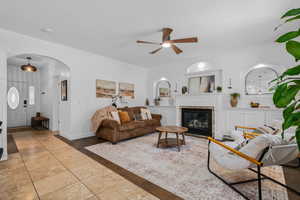 Tiled living room featuring arched walkways, a glass covered fireplace, and a ceiling fan