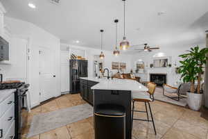 Kitchen featuring two tone cabinets, a glass covered fireplace, black appliances, open floor plan, and a breakfast bar area