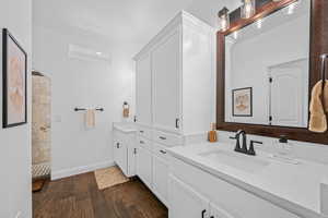 Full bath featuring two vanities, dark wood-style floors, and walk in shower