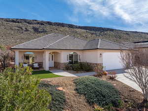 Ranch-style home featuring stone siding, an attached garage, stucco siding, a mountain view, and concrete driveway