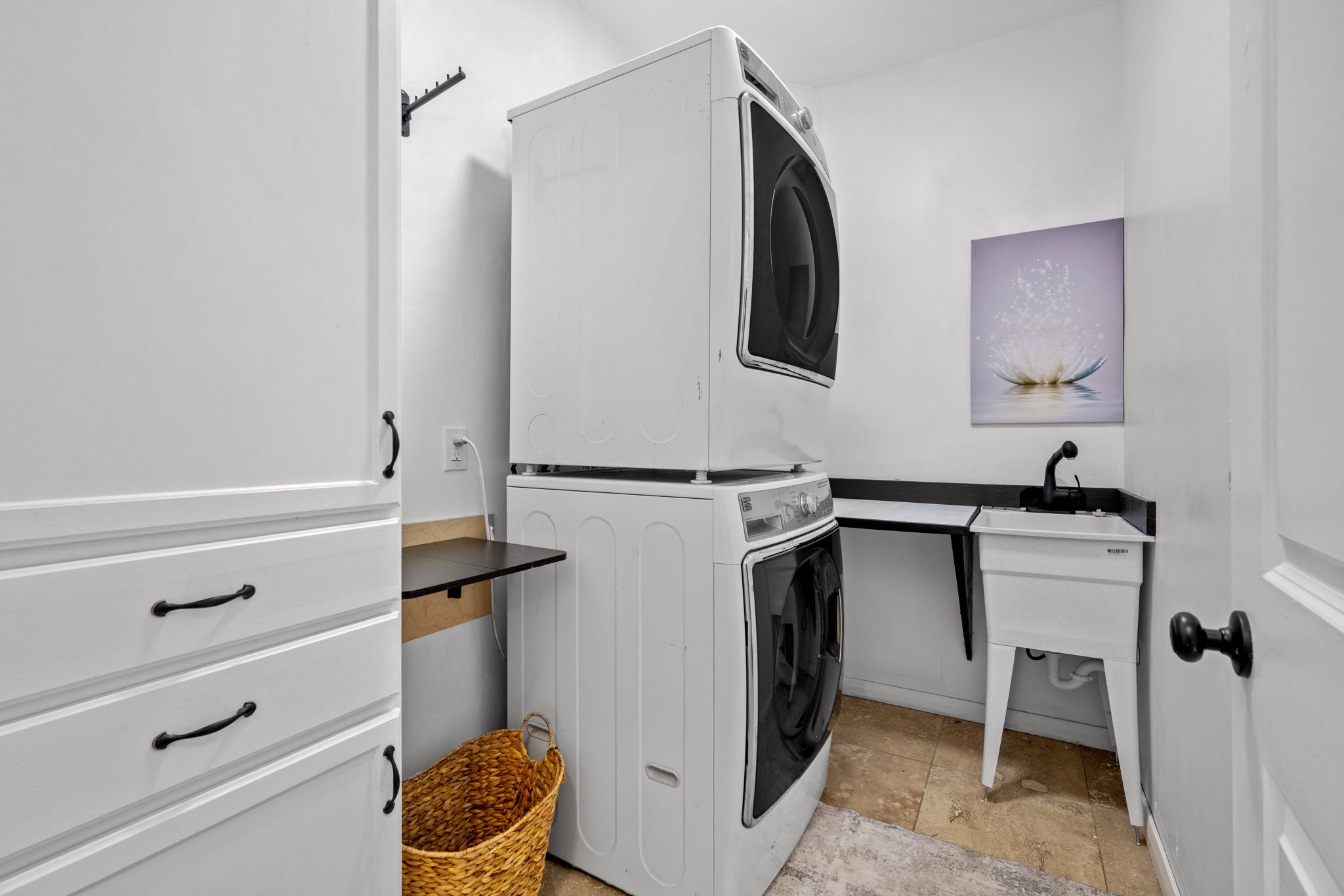 Laundry room with stacked washing machine and dryer and light stone finish floors