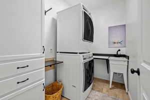 Laundry room with stacked washing machine and dryer and light stone finish floors