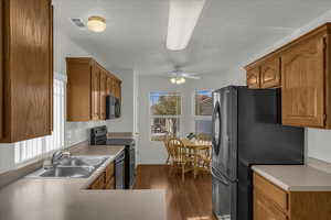 Kitchen with black appliances, wood finish cabinets, dark wood-style flooring, light countertops, and ceiling fan