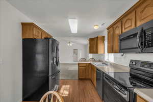 Kitchen with black appliances, lofted ceiling, light countertops, light wood-type flooring, and wood finish cabinetry
