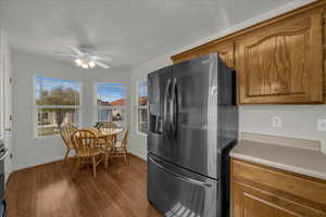 Kitchen with refrigerator with ice dispenser, wood finish cabinetry, light countertops, ceiling fan, and dark wood-style flooring