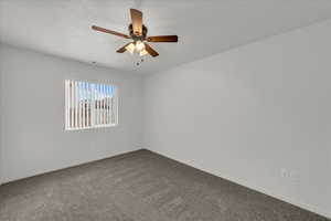 Spare room featuring dark colored carpet and ceiling fan