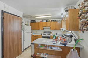 Kitchen featuring a peninsula, light countertops, wood finish cabinetry, white appliances, and a textured ceiling