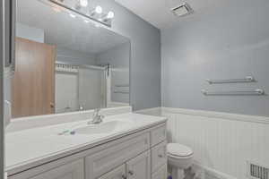 Bathroom featuring wainscoting, vanity, a textured ceiling, and a shower stall