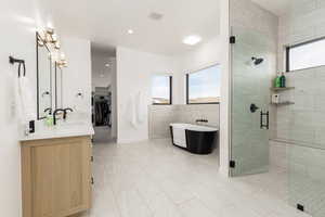 Full bath featuring healthy amount of natural light, a shower stall, double vanity, a walk in closet, and tile walls