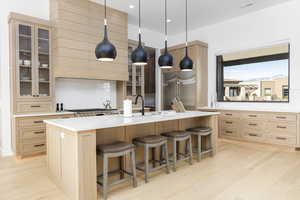 Kitchen with light wood finished floors, glass fronted cabinets, a large island, and light wood finish cabinetry