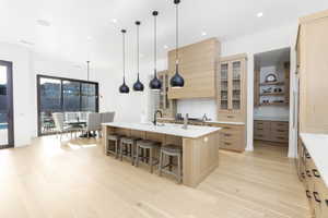 Kitchen with light wood finish cabinetry, glass insert cabinets, a kitchen breakfast bar, a large island, and decorative light fixtures