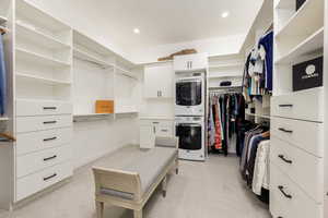 Walk in closet featuring stacked washer / drying machine and light carpet