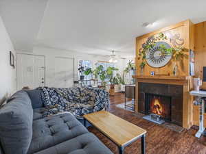 Living room with dark wood-style floors, a tile fireplace, and a ceiling fan