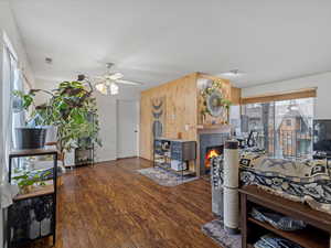 Living area featuring dark wood-style flooring, wooden walls, ceiling fan, and a tile fireplace