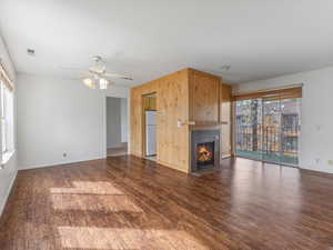 Unfurnished living room featuring dark wood-style floors, a ceiling fan, and a tiled fireplace