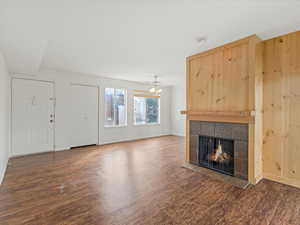 Unfurnished living room with a tile fireplace, dark wood-type flooring, and a ceiling fan